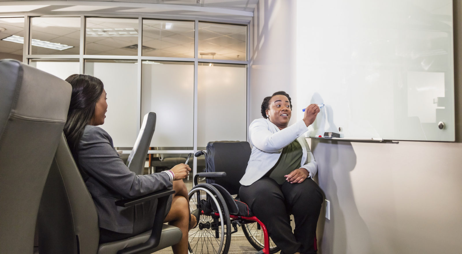 Two African-American businesswomen having a meeting in a boardroom, one in a wheelchair and one in a chair
