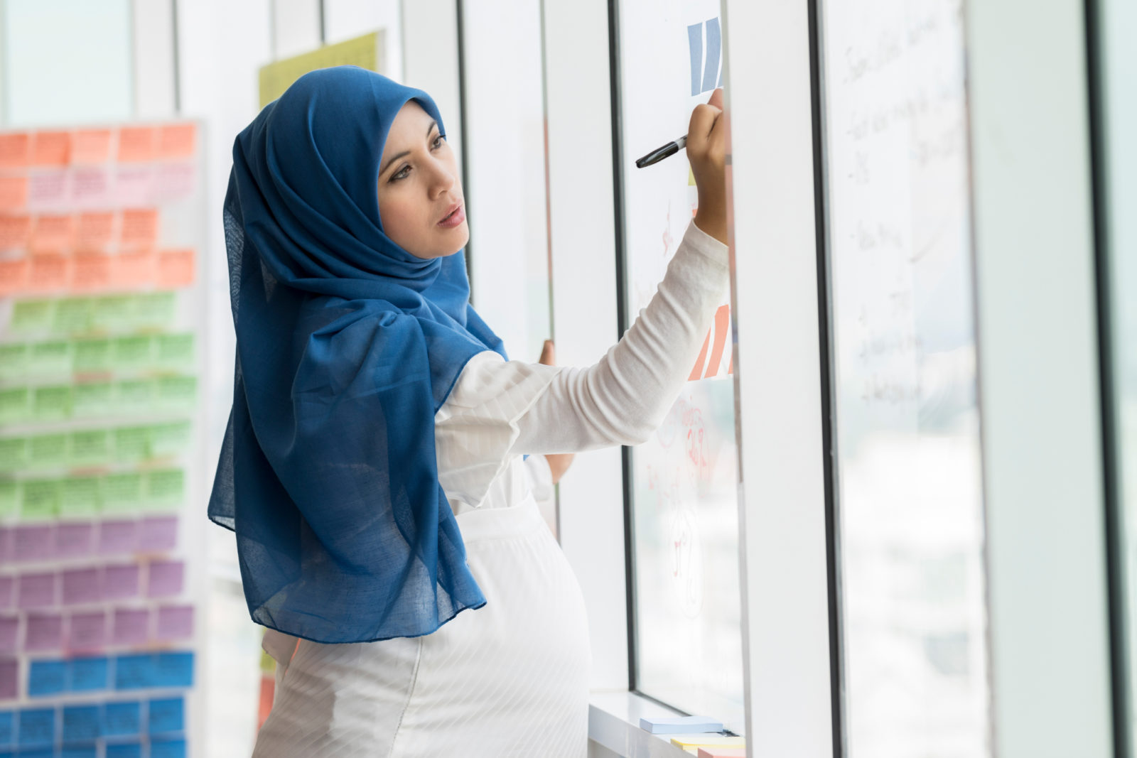 Businesswoman in hijab writes ides on adhesive notes on office window